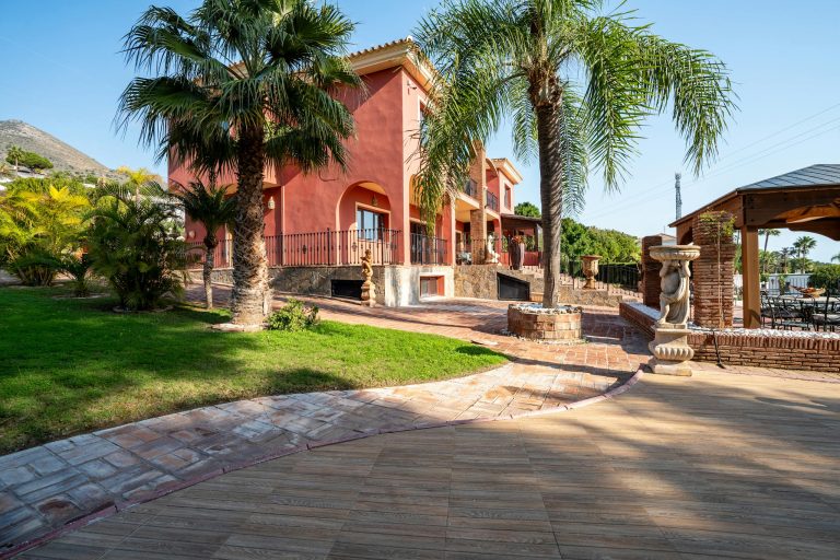 Elegant Mediterranean villa with palm trees and garden in a sunny outdoor setting.